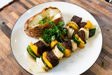 Steak Kebabs, arrangged on a plate with a baked potato.